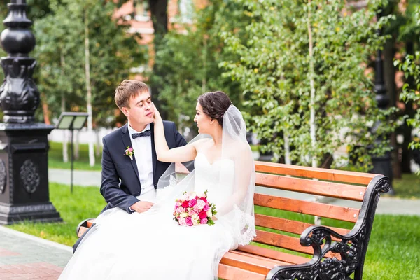 Свадебная пара обнимается, невеста держит букет цветов, жених обнимает ее на улице — стоковое фото