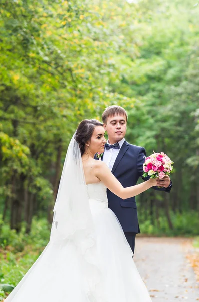 Mariée et marié le jour du mariage marchant à l'extérieur. Heureux jeunes mariés embrassant. Couple aimant . — Photo