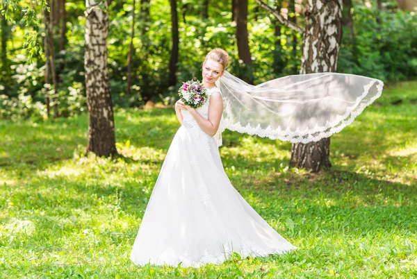 Açık havada uzun örtü ile zarif beyaz elbiseli güzel genç gelin portresi