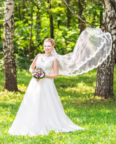 Açık havada uzun örtü ile zarif beyaz elbiseli güzel genç gelin portresi