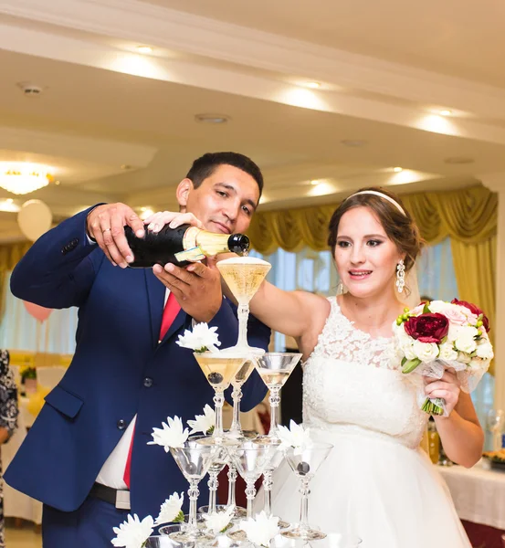 Nevěsta a ženich nalévají šampaňské do sklenice. — Stock fotografie