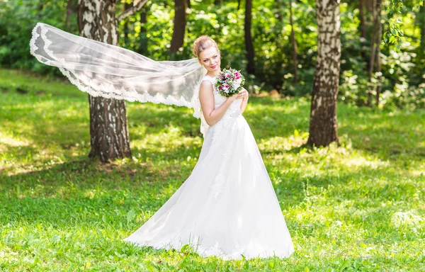 Porträtt av vackra unga brud i elegant vit klänning med lång slöja utomhus — Stockfoto