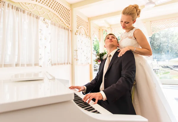 Hochzeitspaar spielt auf einem Klavier im Zimmer — Stockfoto