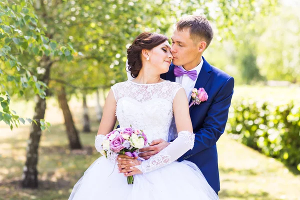 Casamento casal abraçando, a noiva segurando um buquê de flores, noivo abraçando-a ao ar livre — Fotografia de Stock