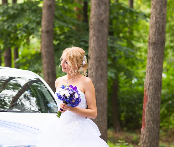 Portret van een mooie blonde bruid met de bruiloft auto. — Stockfoto