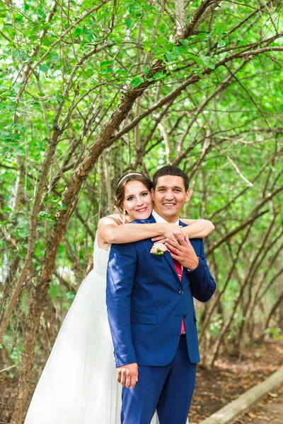 Pareja de boda abrazándose, la novia sosteniendo un ramo de flores, novio abrazándola al aire libre — Foto de Stock