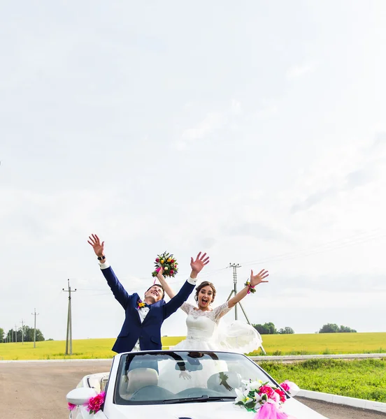 O noivo e a noiva em um carro branco conversível — Fotografia de Stock