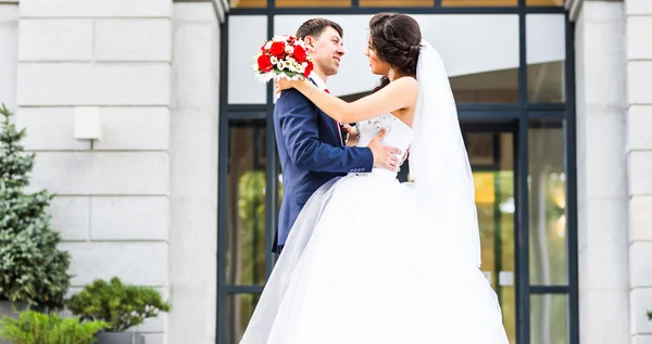 Bruidspaar knuffelen, het houden van een boeket bloemen, bruid bruidegom omarmen haar buitenshuis — Stockfoto