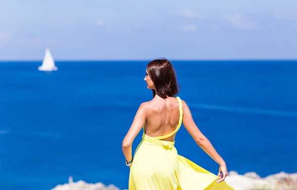 Młoda brunetka kobieta lato żółta sukienka stojąc na plaży i patrząc na morze. — Zdjęcie stockowe