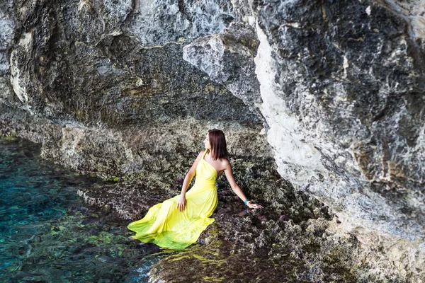 Όμορφη μελαχρινή κοπέλα σε κίτρινο φόρεμα να κάθεται πάνω σε έναν βράχο κοντά στη λίμνη βουνό — Φωτογραφία Αρχείου