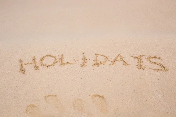 Word vakantie handgeschreven aan zandstrand van tropisch eiland — Stockfoto
