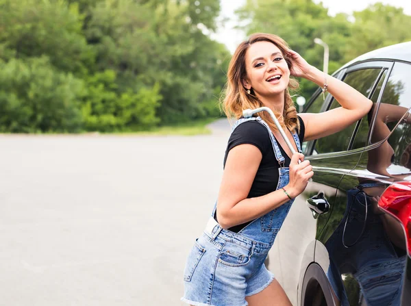 Junge sexy Frau mit Schraubenschlüssel in den Händen und Auto im Hintergrund — Stockfoto