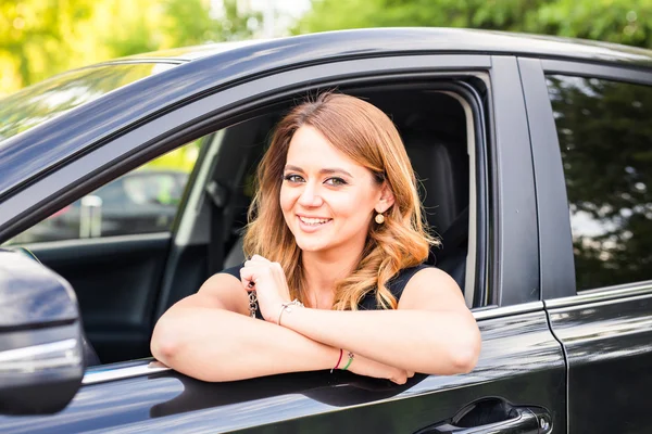 Lächelnde junge hübsche Frau im schwarzen Auto. Reisekonzept, Mietwagen oder Autokauf. — Stockfoto