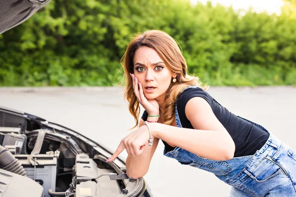 Mujer joven conmocionada mirando el motor debajo del coche de la capucha — Foto de Stock