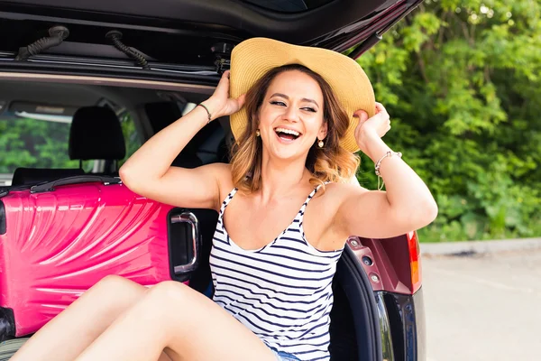 Vrolijke vrouw op zomervakantie reizen zit in de kofferbak van een auto. — Stockfoto