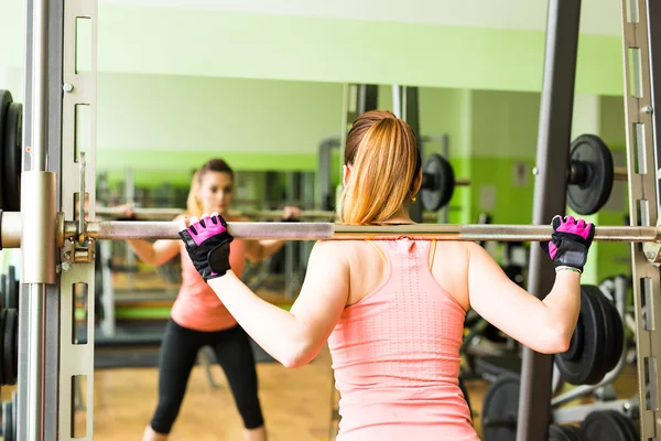 Ung kvinna tränar med skivstång i gymmet — Stockfoto