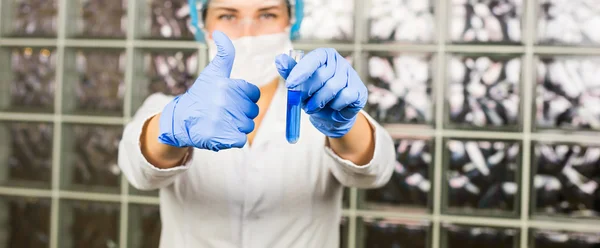 Жінка-лаборант дає великі пальці успіху, тримаючи пробірку в рукавичках — стокове фото