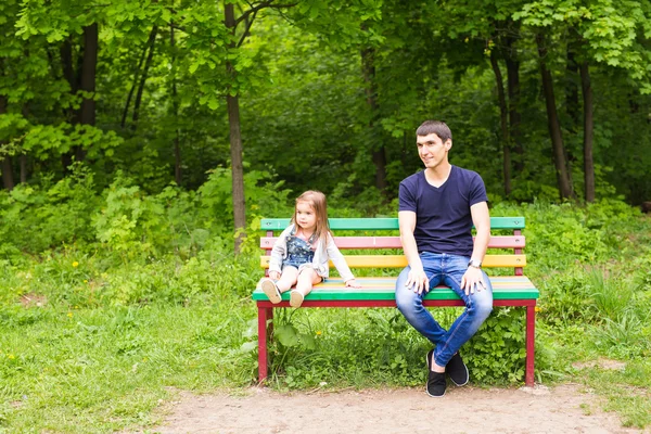 Retrato del padre con la pequeña hija sonriendo y sentado en el banco de madera en el parque de verano — Foto de Stock