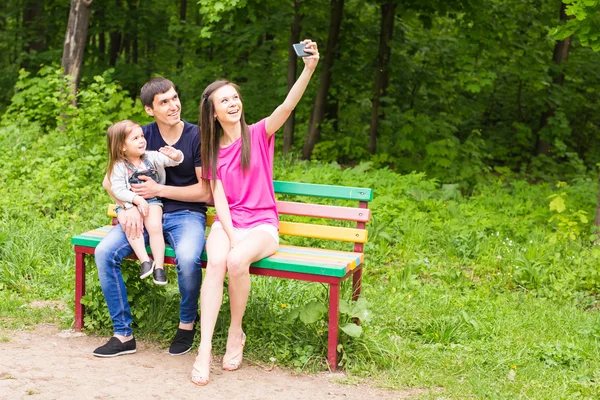 Sommar scen av glada unga familjen som selfies med sin smartphone i parken — Stockfoto