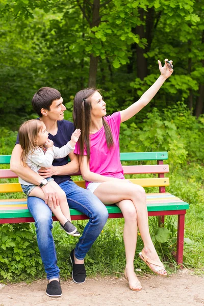 Sommar scen av glada unga familjen som selfies med sin smartphone i parken — Stockfoto