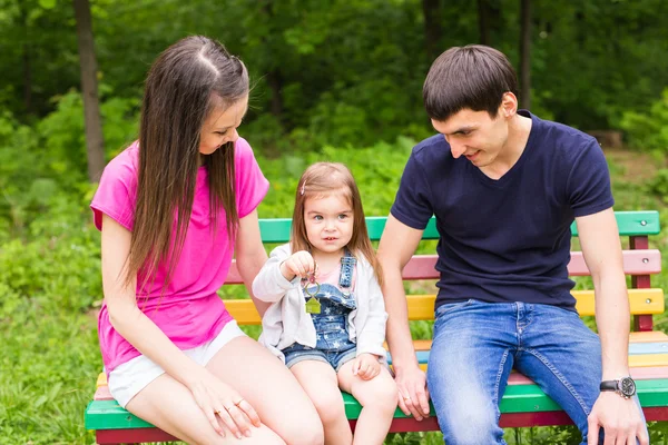 Familia joven sentada en un banco en el parque de verano — Foto de Stock