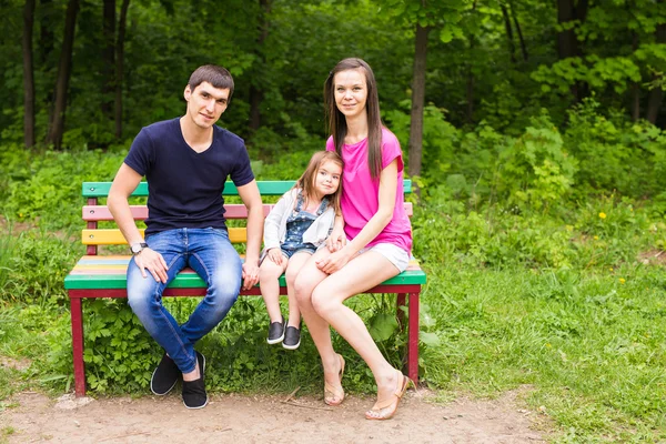 Młoda rodzina siedzi na ławce w parku lato — Zdjęcie stockowe