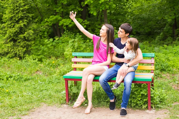 Sommar scen av glada unga familjen som selfies med sin smartphone i parken — Stockfoto
