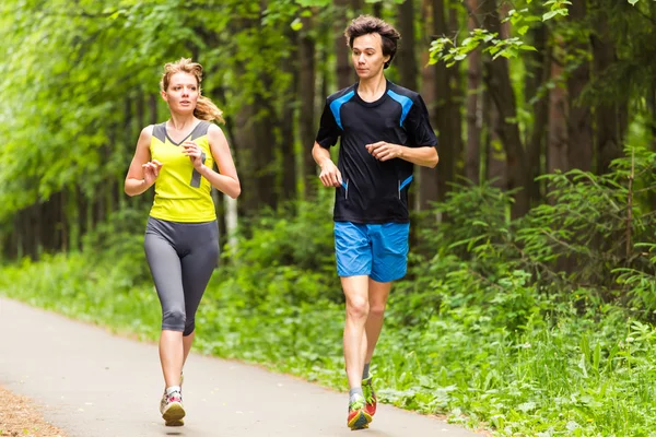 Un couple qui court dehors. Femme et homme coureurs jogging ensemble à l'extérieur dans toute la longueur du corps . — Photo