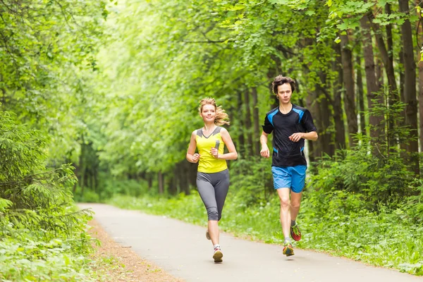 Un couple qui court dehors. Femme et homme coureurs jogging ensemble à l'extérieur dans toute la longueur du corps . — Photo