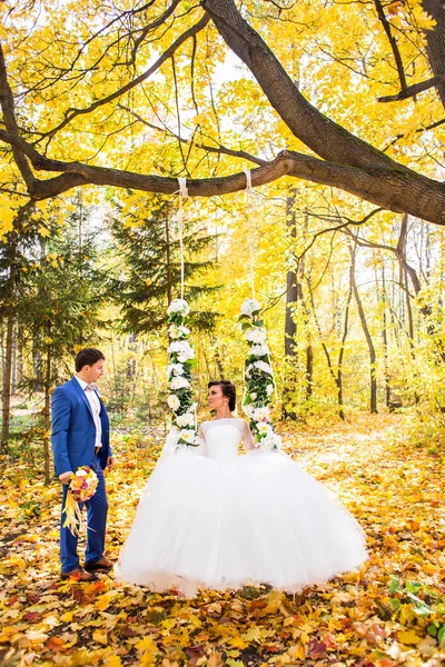 A noiva e o noivo em um balanço no parque de outono — Fotografia de Stock