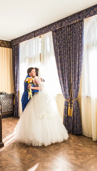 Noiva de luxo feliz e noivo de pé na luz da janela em quarto rico — Fotografia de Stock