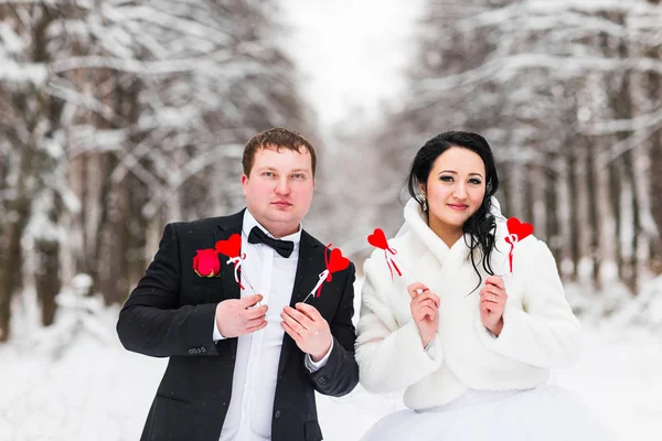 Novia y novio sosteniendo corazones de papel en el parque de invierno — Foto de Stock