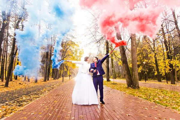 Pareja de boda con humo de color en el parque de otoño. Bomba de color — Foto de Stock