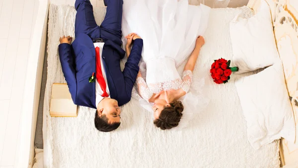 Belo casal recém-casado deitado na cama e de mãos dadas — Fotografia de Stock