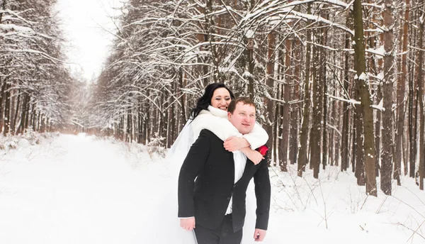 Mann gibt Frau Huckepackfahrt im Winterurlaub im verschneiten Wald. — Stockfoto