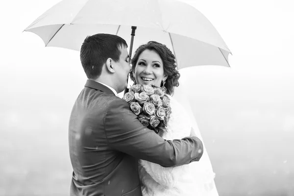 Bride and groom standing under an umbrella. — Stock Photo, Image