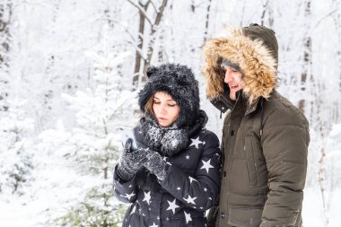 Sezon, aşk, teknoloji ve eğlence konsepti. Mutlu çift kış arkaplanı boyunca akıllı telefonla selfie çekiyor.