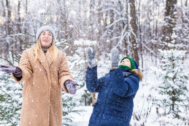 Ebeveynlik, eğlence ve sezon konsepti - Mutlu anne ve oğul kış ormanlarında kar ile oynayıp eğleniyorlar
