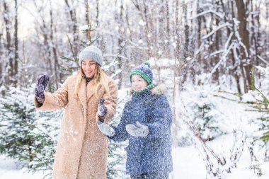 Ebeveynlik, eğlence ve sezon konsepti - Mutlu anne ve oğul kış ormanlarında kar ile oynayıp eğleniyorlar