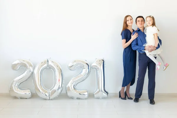 Joven familia feliz madre y padre e hija de pie cerca de globos en forma de números 2021 sobre fondo blanco. Año nuevo, Navidad, vacaciones — Foto de Stock