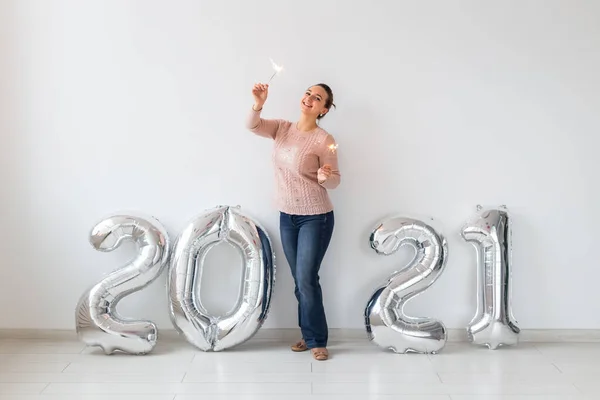 Celebración de Año Nuevo y concepto de fiesta - Mujer joven feliz con brillantes cerca de plata 2021 globos sobre fondo blanco. — Foto de Stock