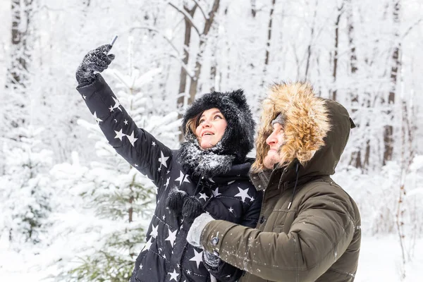 Saison, amour, technologie et concept de loisirs - couple heureux prenant selfie par smartphone sur fond d'hiver — Photo