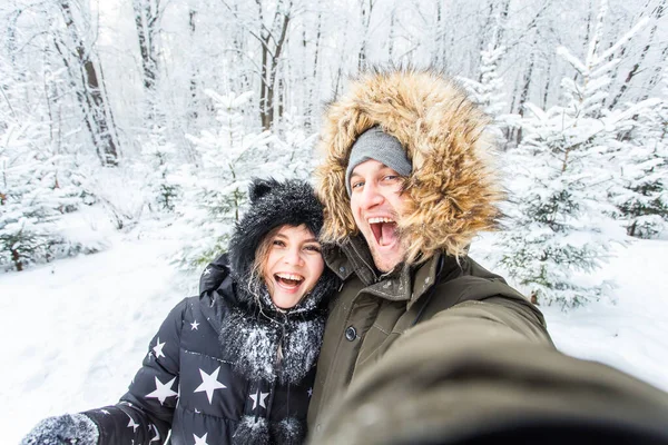 Technologies et concept de relation - Couple souriant heureux prenant un selfie dans une forêt d'hiver à l'extérieur — Photo
