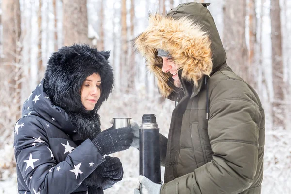 Sezon i koncepcja spaceru - Szczęśliwa para pije gorącą herbatę w zimowym lesie — Zdjęcie stockowe