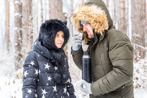 Concepto de temporada y paseo - Pareja feliz bebiendo té caliente en el bosque de invierno — Foto de Stock