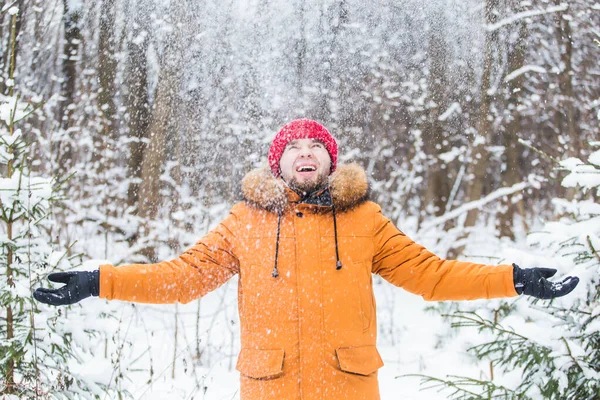 Young man throwing snow in winter forest. Guy having fun outdoors. Winter activities.