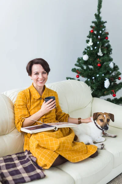 Γυναίκα διαβάζει το βιβλίο μπροστά από το χριστουγεννιάτικο δέντρο με σκυλί Jack Russell τεριέ. Χριστούγεννα, διακοπές και κατοικίδια ζώα. — Φωτογραφία Αρχείου