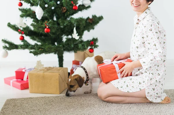 Ευτυχισμένη γυναίκα με σκύλο να ανοίγει χριστουγεννιάτικα δώρα. Χριστουγεννιάτικο δέντρο με δώρα από κάτω. Διακοσμημένο σαλόνι. Κοντινό πλάνο. — Φωτογραφία Αρχείου
