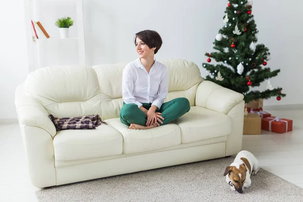Šťastná mladá žena s krásným psem v obývacím pokoji s vánoční stromeček. Koncept dovolených. — Stock fotografie