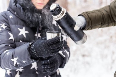 Termos ve soğuk sezon konsepti. Bir kadın sıcak içecek koyar. Kış tatilinde bir çift